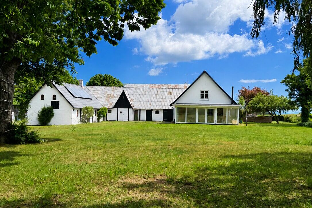 Der Hof auf Bornholm — weiße Gebäude inmitten von Natur, mit Teich und alten Bäumen